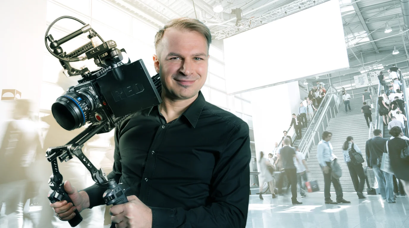 Kameramann von Eigenart Filmproduktion mit RED-Kamera auf dem Schulterstativ in einer Messehalle